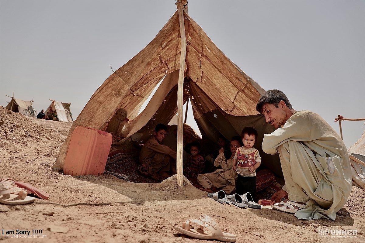 A father crouching beside his children sheltering in a makeshift tent