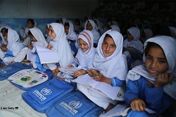 Smiling schoolgirls in white headscarves studying with UNHCR school bags